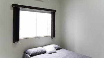Quarto com cama, janela com persianas e ar condicionado na parede.