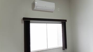 Una habitación con ventana, aire acondicionado de pared y marco de ventana oscuro.