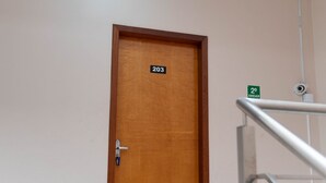 Puiset ovet, joissa on numerokilpi, metallinen kaide ja turvakamera.