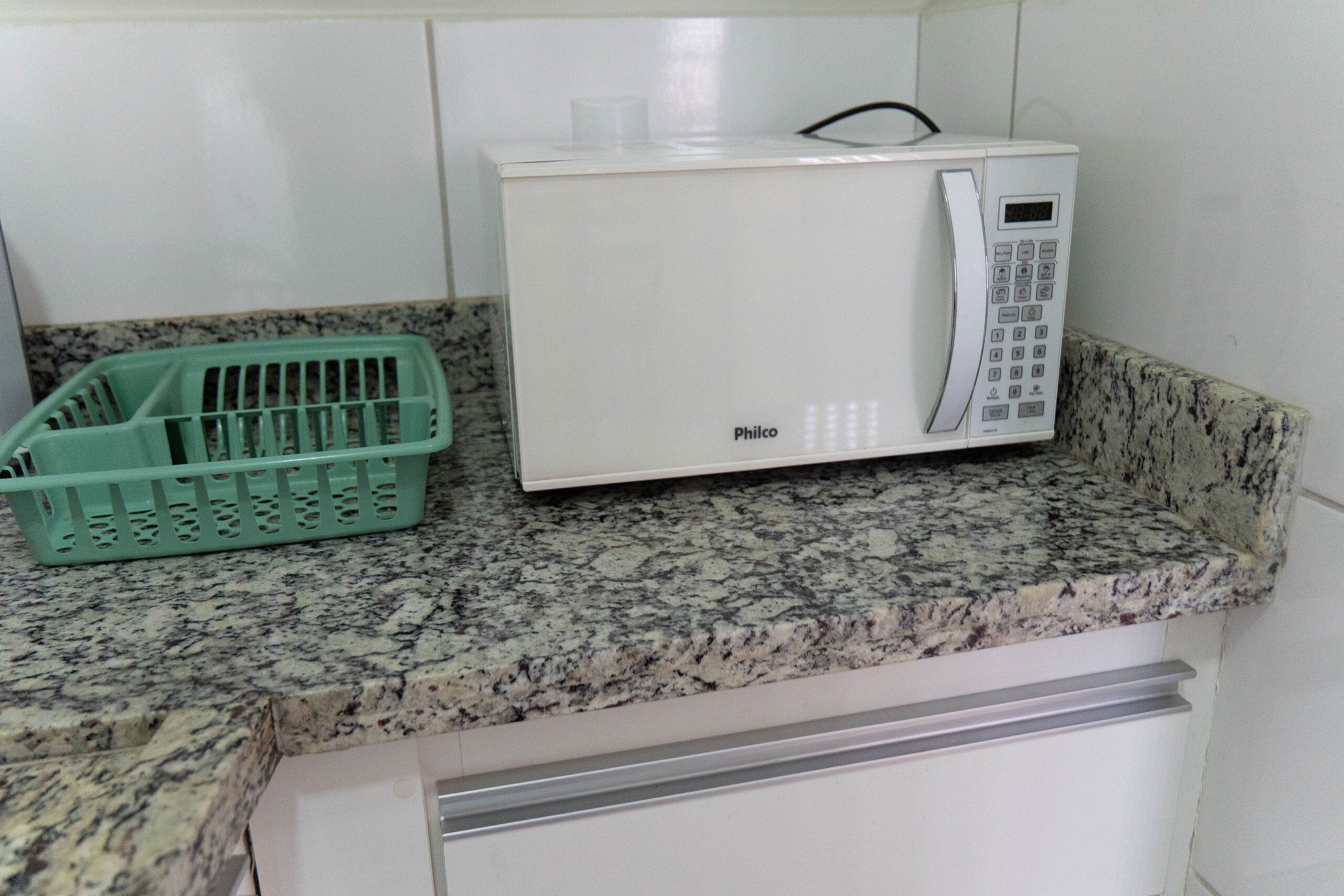 Un microondas sobre una encimera de granito con una cesta verde a su lado.