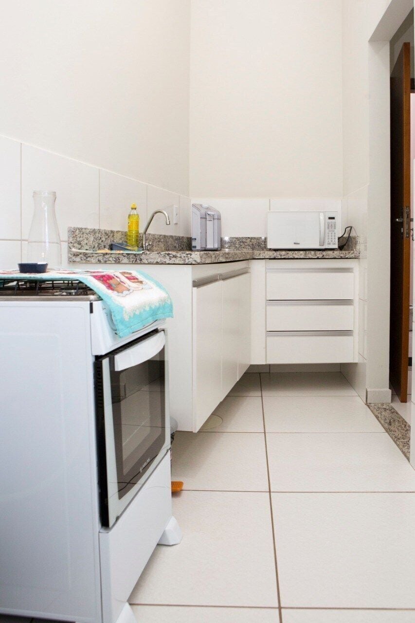 Uma cozinha compacta com armários brancos, micro-ondas, torradeira e fogão a gás.