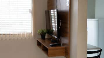 Un televisor montado en un estante de madera, con un control remoto y una planta en maceta a su lado.