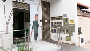 Entrada de um edifício com uma porta verde, uma câmera de segurança e vários caixas de correio numerados na parede.