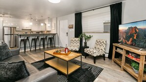 Un appartement moderne comprenant une cuisine, un coin repas et un salon. Il est équipé d’un canapé, d’une table basse et d’un meuble pour la télévision avec un écran plat.