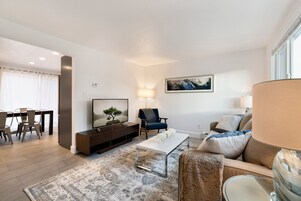 Una sala de estar moderna con una televisión de pantalla plana, un sofá, una mesa de centro y un comedor con sillas.