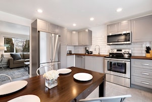 Una cocina moderna con electrodomésticos de acero inoxidable, armarios blancos y una mesa de comedor de madera.