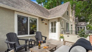 A covered patio with outdoor seating, including two Adirondack chairs and a wooden table with a bottle and glasses.