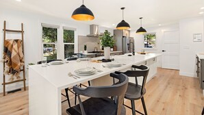 A modern kitchen with a central island, pendant lighting, and a view of the outdoors through large windows.