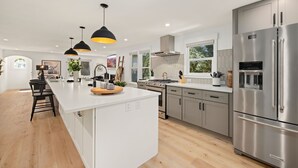 A modern kitchen with a large island, stainless steel appliances, pendant lighting, and a view of the outdoors.