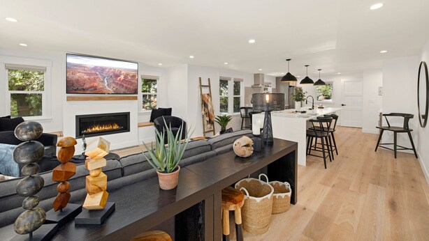A modern living room with a fireplace, a large TV, and a dining area with a kitchen in the background.