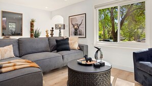 A modern living room with a grey sectional sofa, a round coffee table, and a large window with a view of trees.