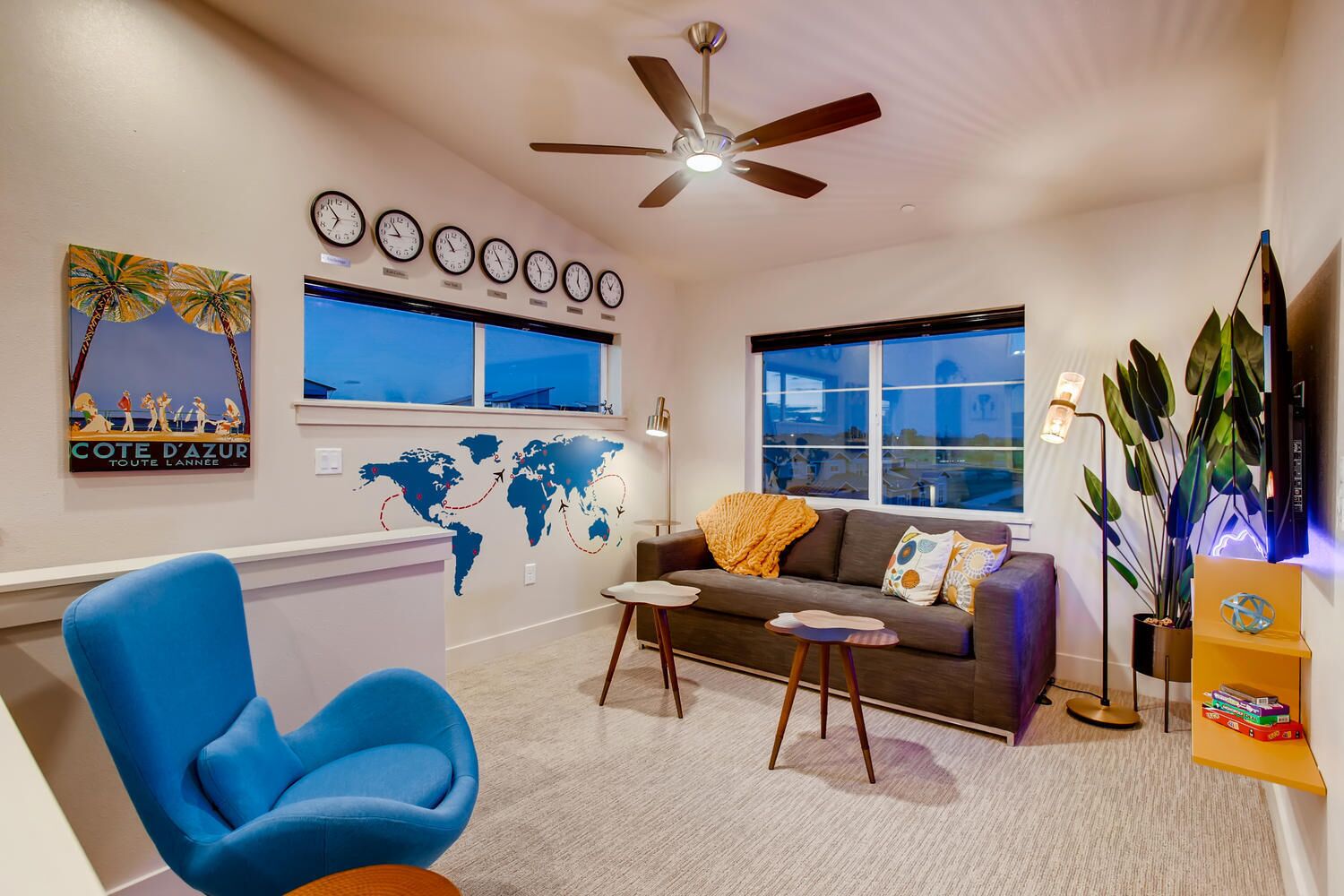 A modern living room with a blue chair, a sofa, a coffee table, a world map wall, and a ceiling fan.