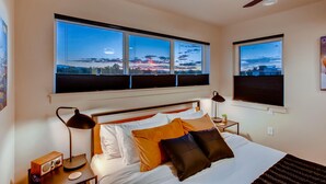 Une chambre d’hôtel avec un lit, une table de chevet, une lampe et une vue sur le paysage urbain, visible à travers de grandes fenêtres.