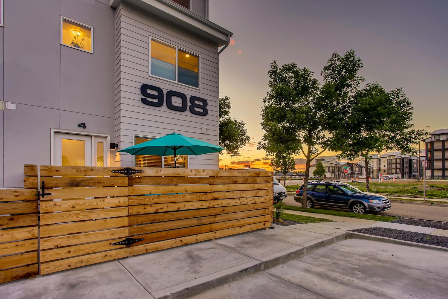 Un bâtiment moderne avec le numéro 908 sur la façade, une clôture en bois et une voiture garée.