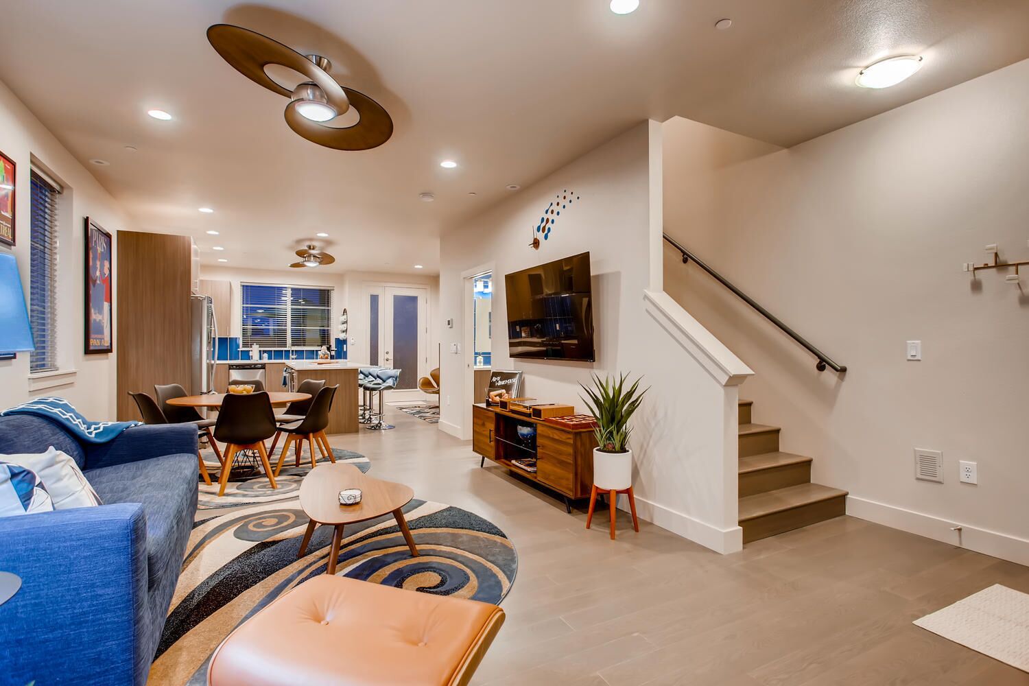 A modern living room with a sofa, coffee table, and dining area. There is a staircase leading to another level.