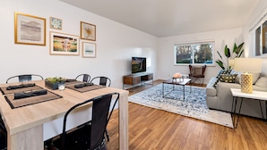 A modern living room with a wooden dining table, black chairs, a TV, and a sofa. - Urban Oasis Near Old Town & Pvh – Dog Friendly! (Fort Collins)