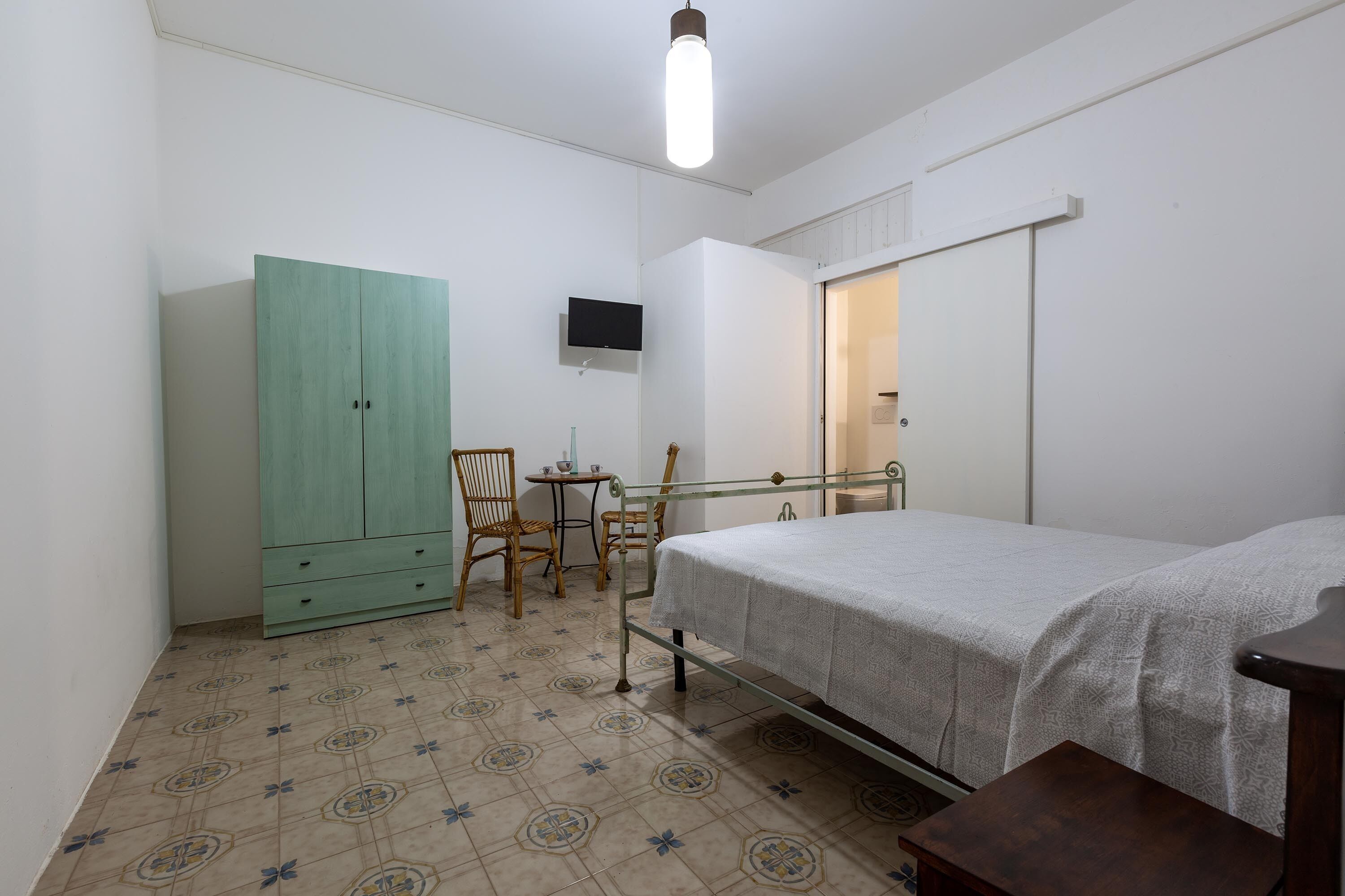 A bedroom with a bed, a wardrobe, a TV mounted on the wall, and a small table with chairs.