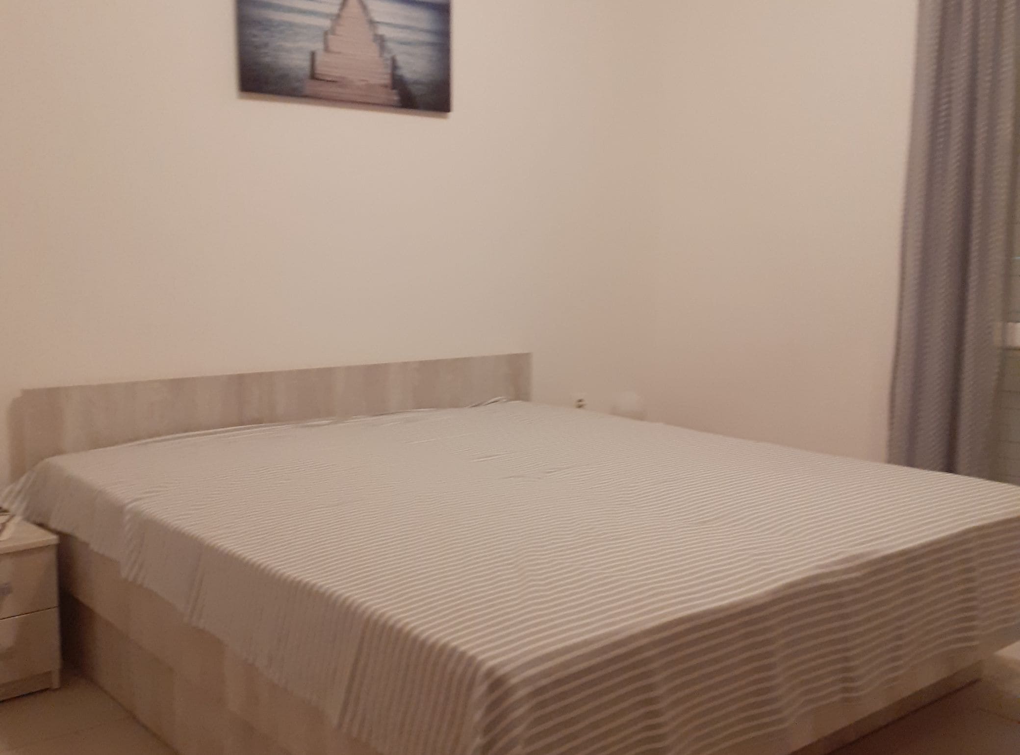 A single bed with a striped bedspread, a nightstand, and a wall-mounted picture.