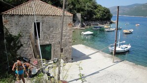 A stone building with a tiled roof near a body of water with boats. - Apartments Ane (Konavle)