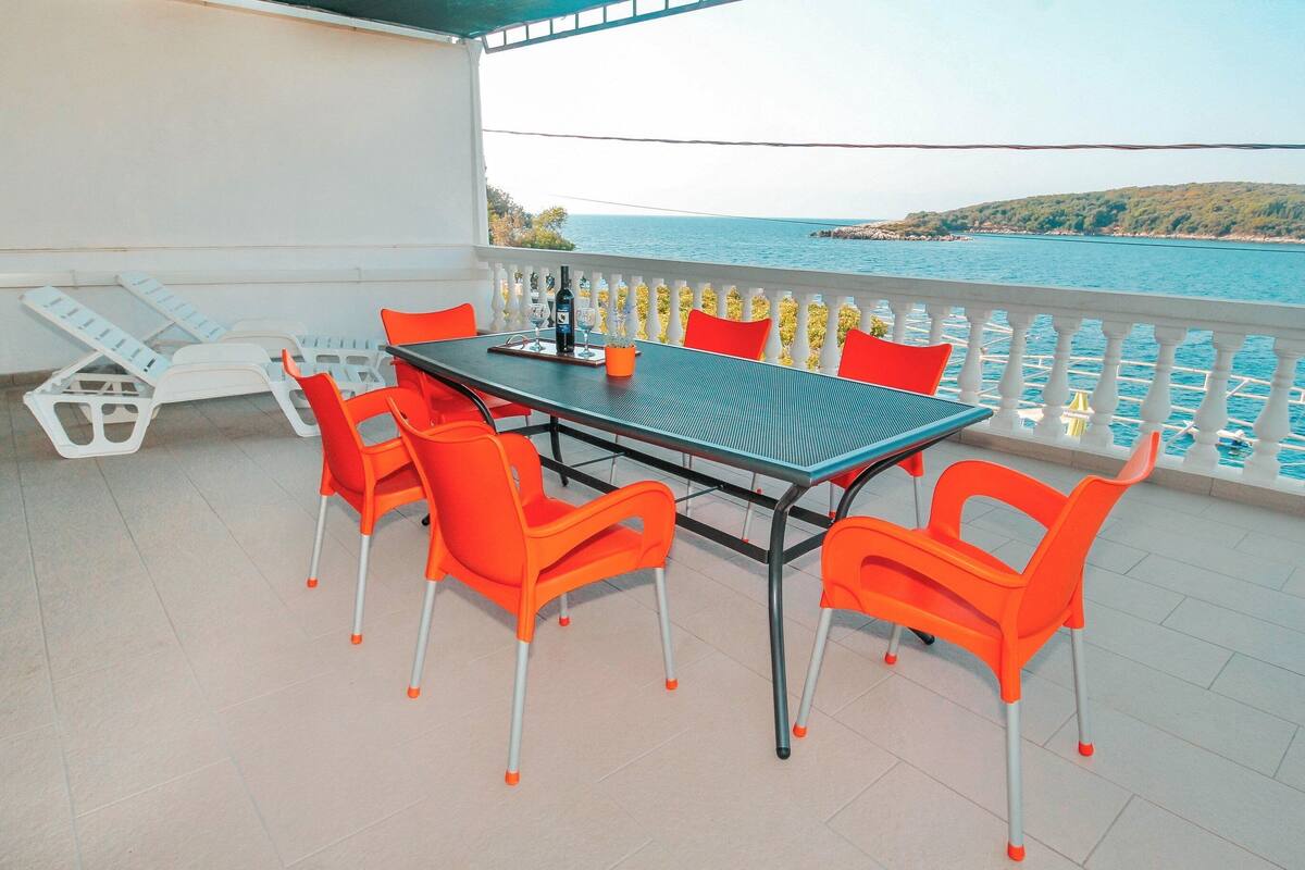 A balcony with a table and chairs, overlooking a body of water and a hilly landscape.