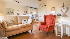 Una sala de estar con un sofá, un sillón rojo, una mesita con una lámpara, y una cocina al fondo.