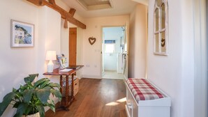 Un pasillo acogedor con vigas de madera, un banco, una mesa con revistas, un adorno con forma de corazón y una ventana con cortinas.