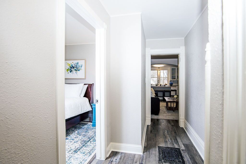 Un pasillo que conduce a un dormitorio con cama y mesita de noche, una zona de comedor con mesa y sillas, y una cocina visible al fondo.