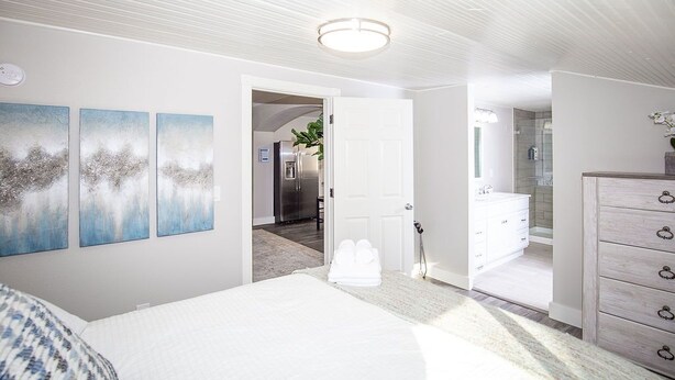 A bedroom with a bed, a dresser, and a bathroom visible through an open door. - Couples Getaway | Walk to Unc | Free Cruiser Bikes (Greeley)