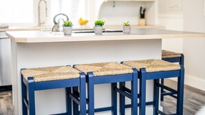 A kitchen with a central island, three blue bar stools with woven seats, and small potted plants on the island. - Couples Getaway | Walk to Unc | Free Cruiser Bikes (Greeley)