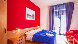 A modern hotel room with a wooden wardrobe, a bed with blue bedding, a red chair, and a large window with purple curtains. - Mammasisi (Lecce)