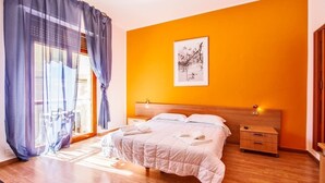 A bedroom with a bed, a nightstand, a wooden headboard, a window with curtains, and a wall-mounted artwork. - Mammasisi (Lecce)