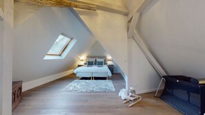 Una camera da letto con soffitto spiovente, un lucernario, un letto con cuscini, un comodino, un piccolo tappeto e un orsacchiotto su una slitta.