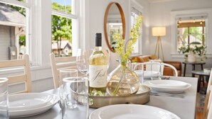A dining table set with white plates, glasses, and a bottle of wine.
