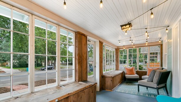 A covered porch with large windows, wooden benches, and seating areas.