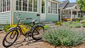 A green house with a number 523, a bicycle parked in front, and a garden with various plants.