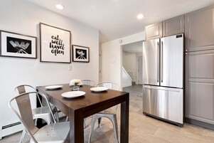 A modern kitchen with stainless steel appliances, a dining table with chairs, and framed inspirational quotes on the wall.