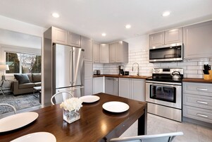 A modern kitchen with stainless steel appliances, white cabinetry, and a wooden dining table.