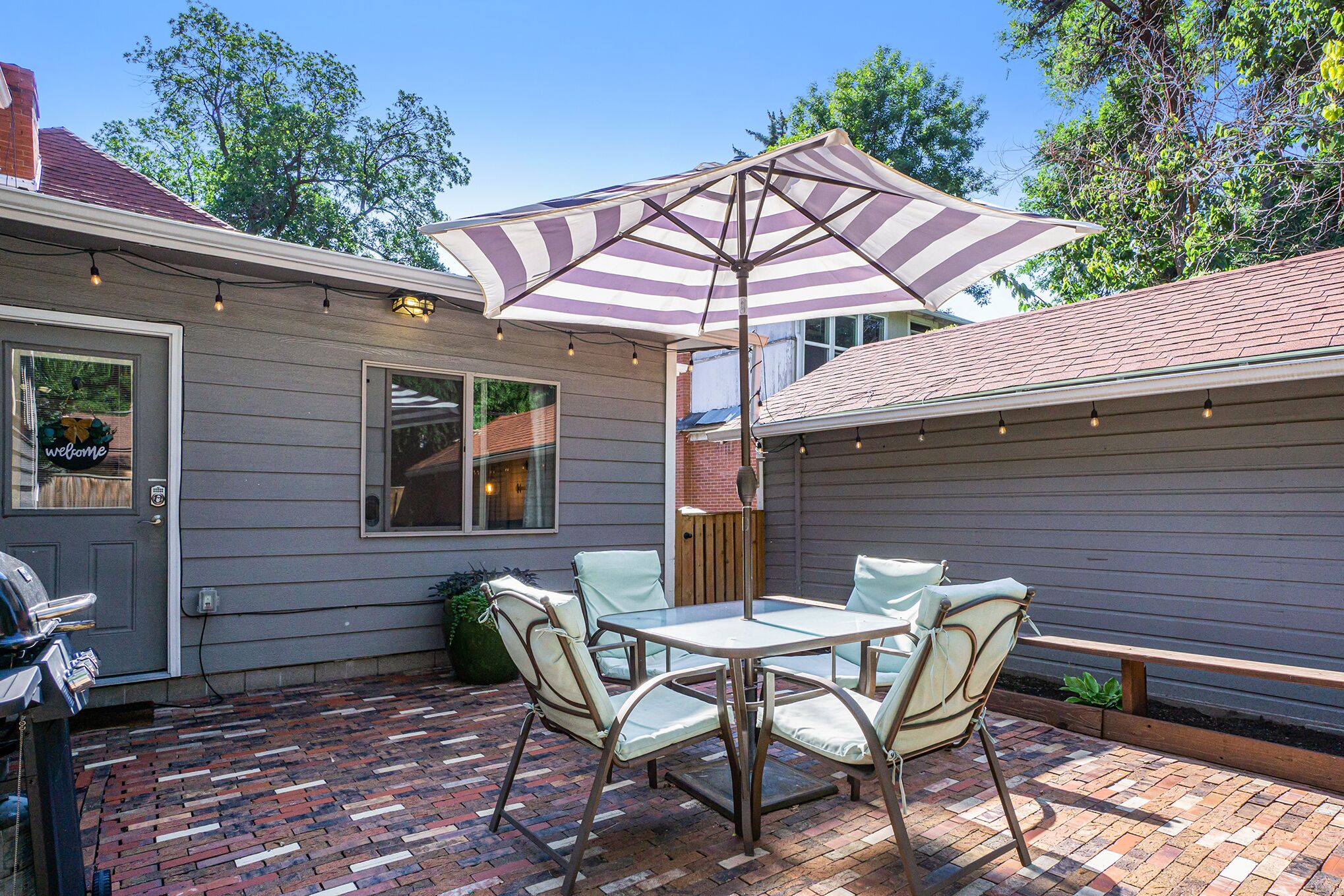 A patio with a brick floor, a table with chairs, and a striped umbrella.