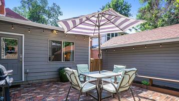 A patio with a brick floor, a table with chairs, and a striped umbrella.