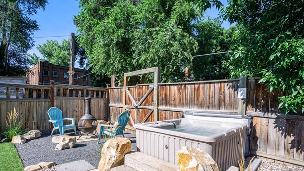 Un jardin avec un jacuzzi, deux chaises Adirondack bleues, une clôture en bois et un chemin de pierres.