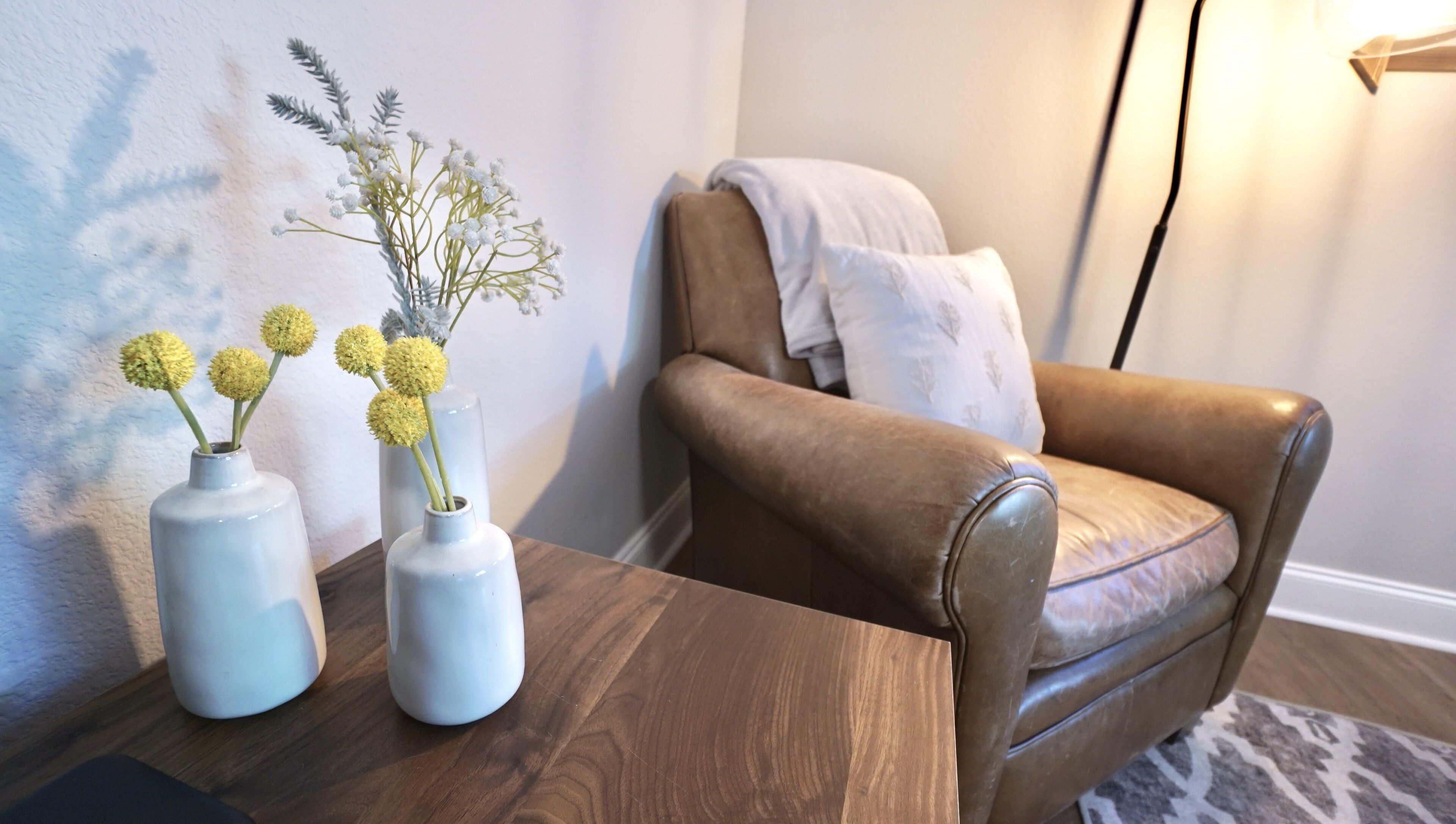 A brown leather armchair with a white cushion, two white vases with yellow flowers, and a wooden table.