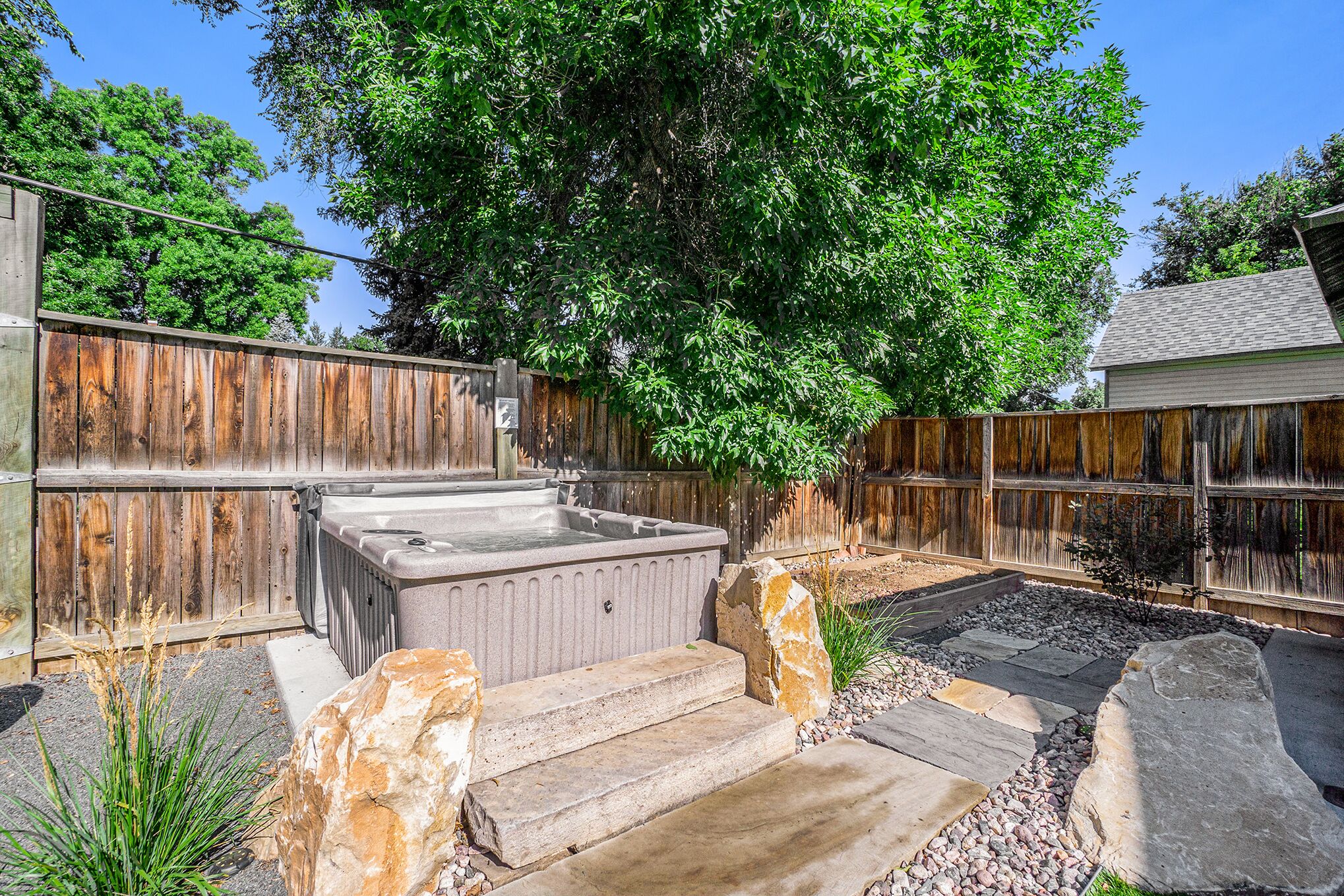 A backyard with a hot tub, stone steps, and a wooden fence.