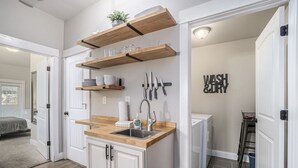 Une cuisine compacte avec des étagères en bois, un évier et une pancarte indiquant « LAVER ET SÉCHER ».