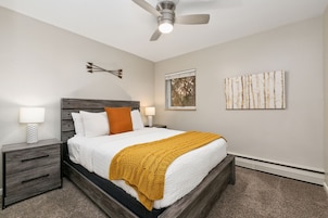 Un dormitorio con cama, mesitas de noche, ventilador de techo y decoración en la pared.