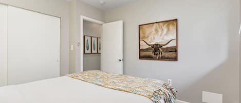 A bedroom with a bed, a door, a ceiling fan, and a wall-mounted painting.