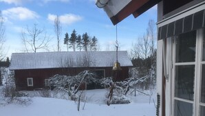 Un espace extérieur enneigé avec un banc en bois et un bâtiment rouge en arrière-plan.