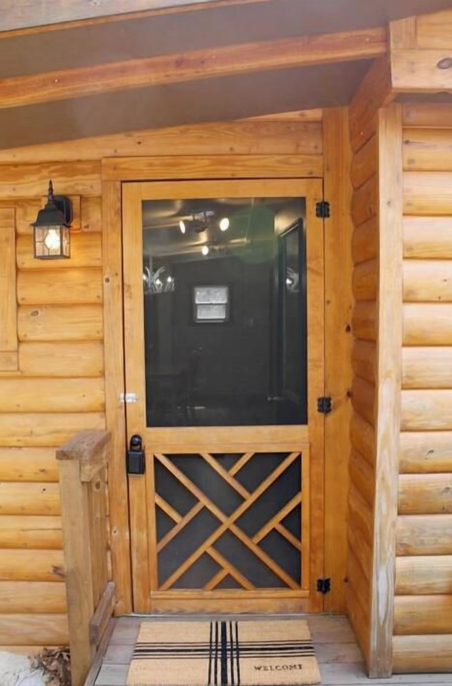 Een houten chalet-ingang met een glazen deur, een deurmat en een lantaarn.