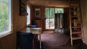 Ein gemütliches Blockhaus-Interieur mit Holzvertäfelung, einem Schreibtisch mit Stuhl, einem Bücherregal und einem großen Fenster mit Blick ins Freie.