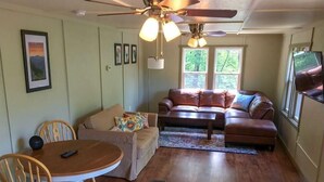 A living room with a brown leather sofa, a round wooden table, and a ceiling fan. - Shenandoah National Park - Sauna - Log Cabin - Treehouse - Game Room (Stanley)