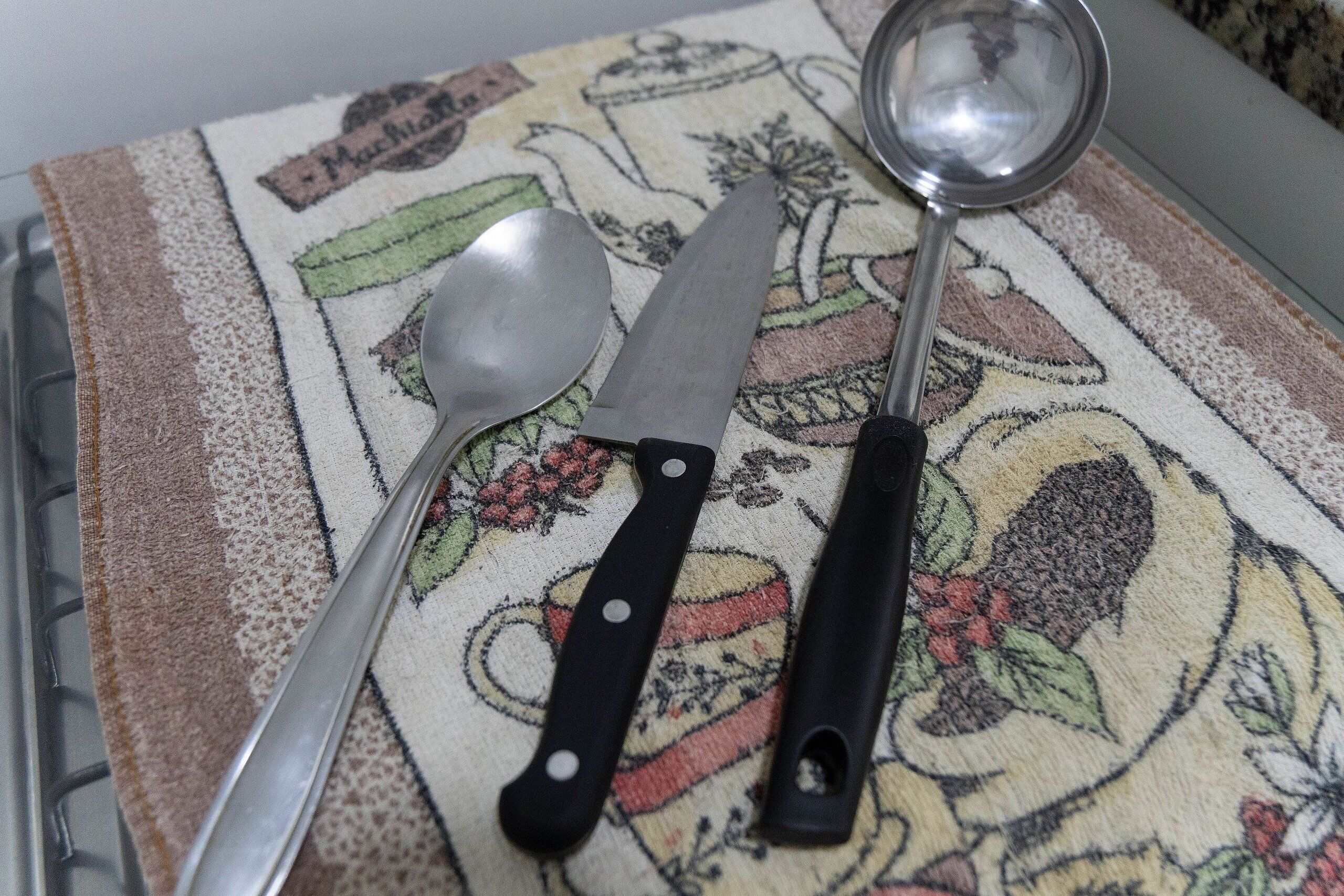 A kitchen area with a metal spoon and a knife on a patterned tablecloth.